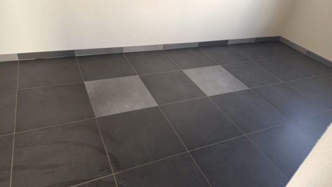 Dunkelgraue Fliesen mit zwei helleren quadratischen Fliesen in der Mitte.